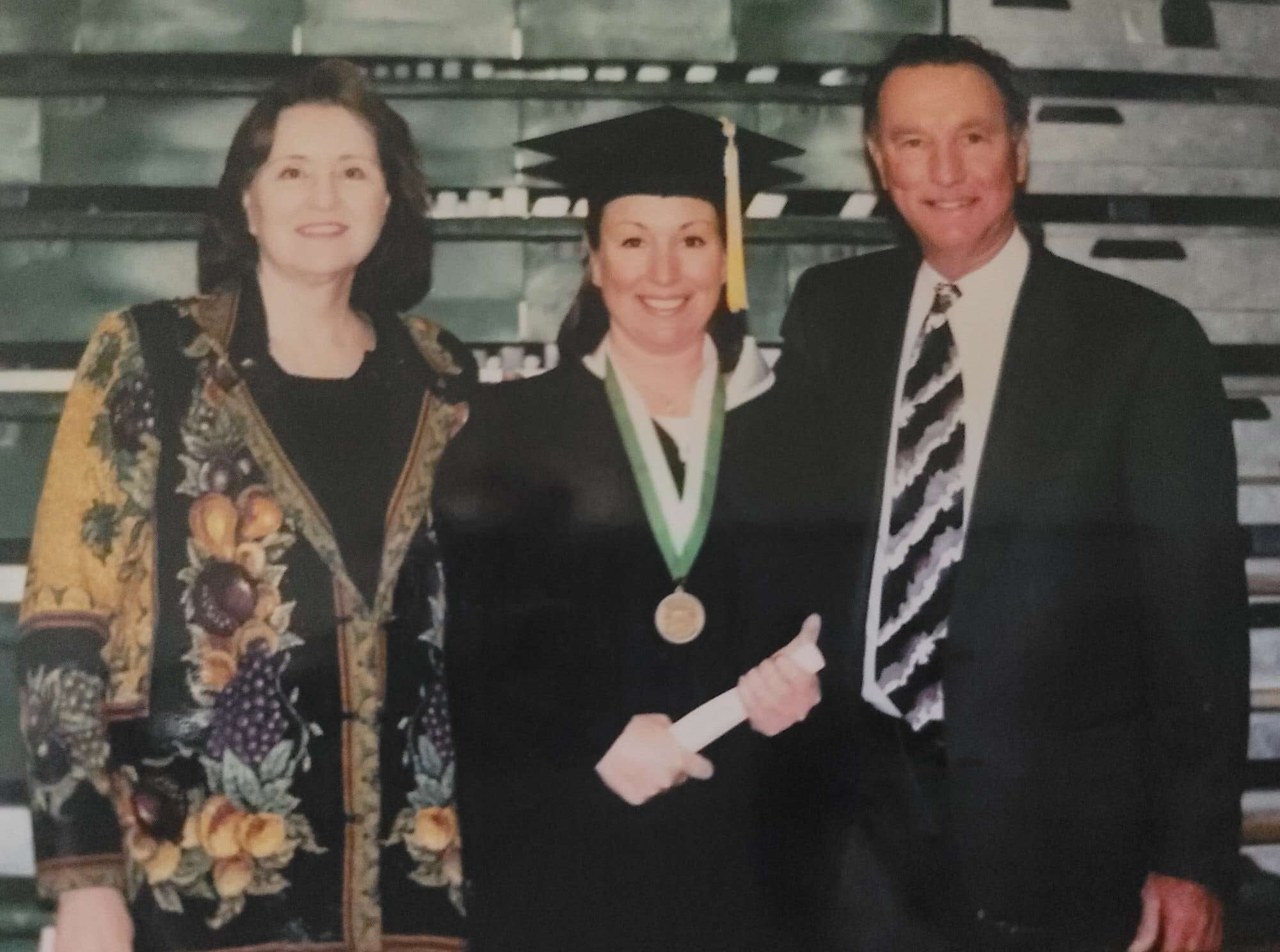 Lisa Lunsford in cap and gown at her University of Texas at Dallas graduation, holding her diploma, standing with family.