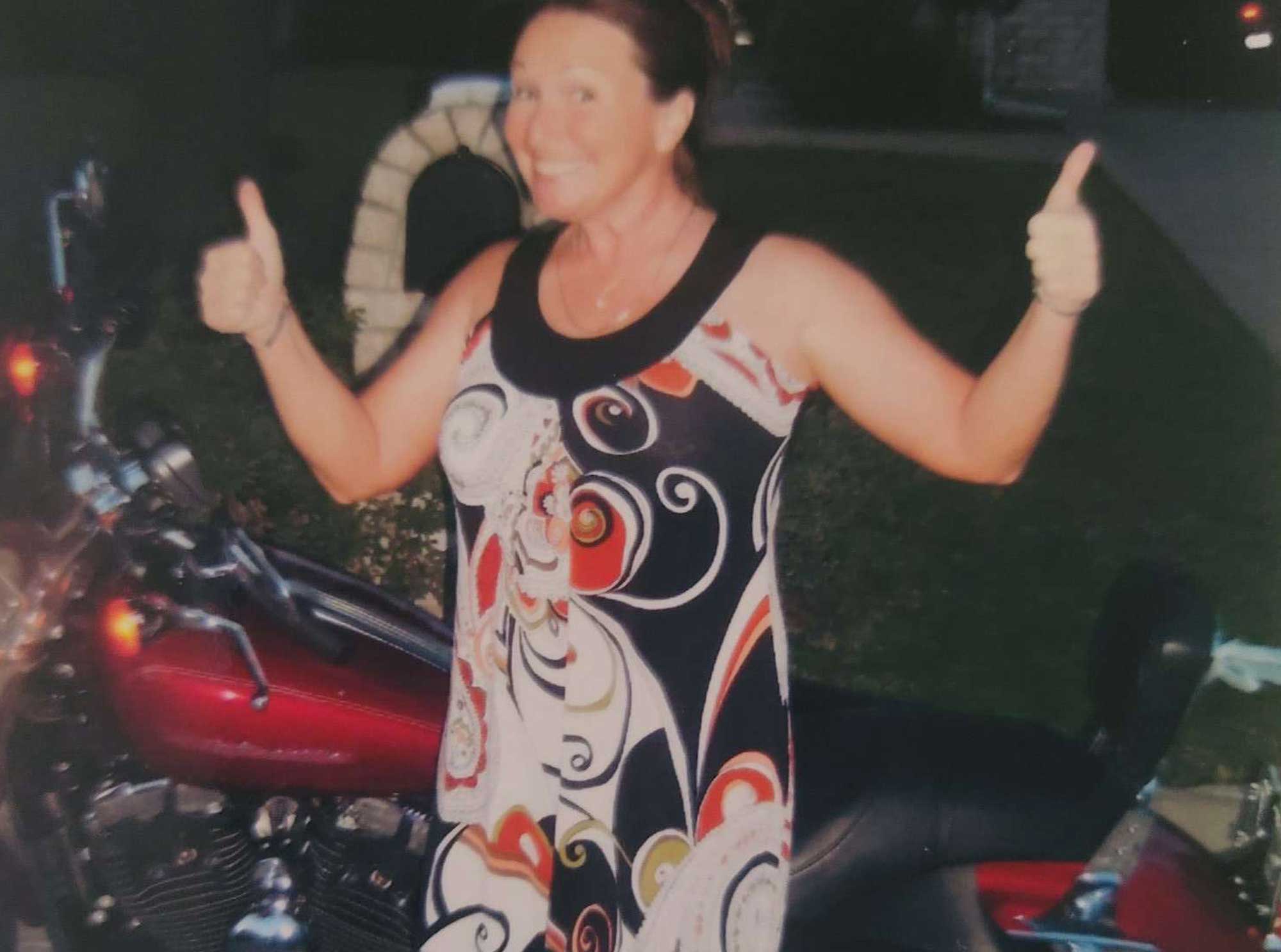 Lisa Lunsford giving two thumbs up beside her motorcycle.